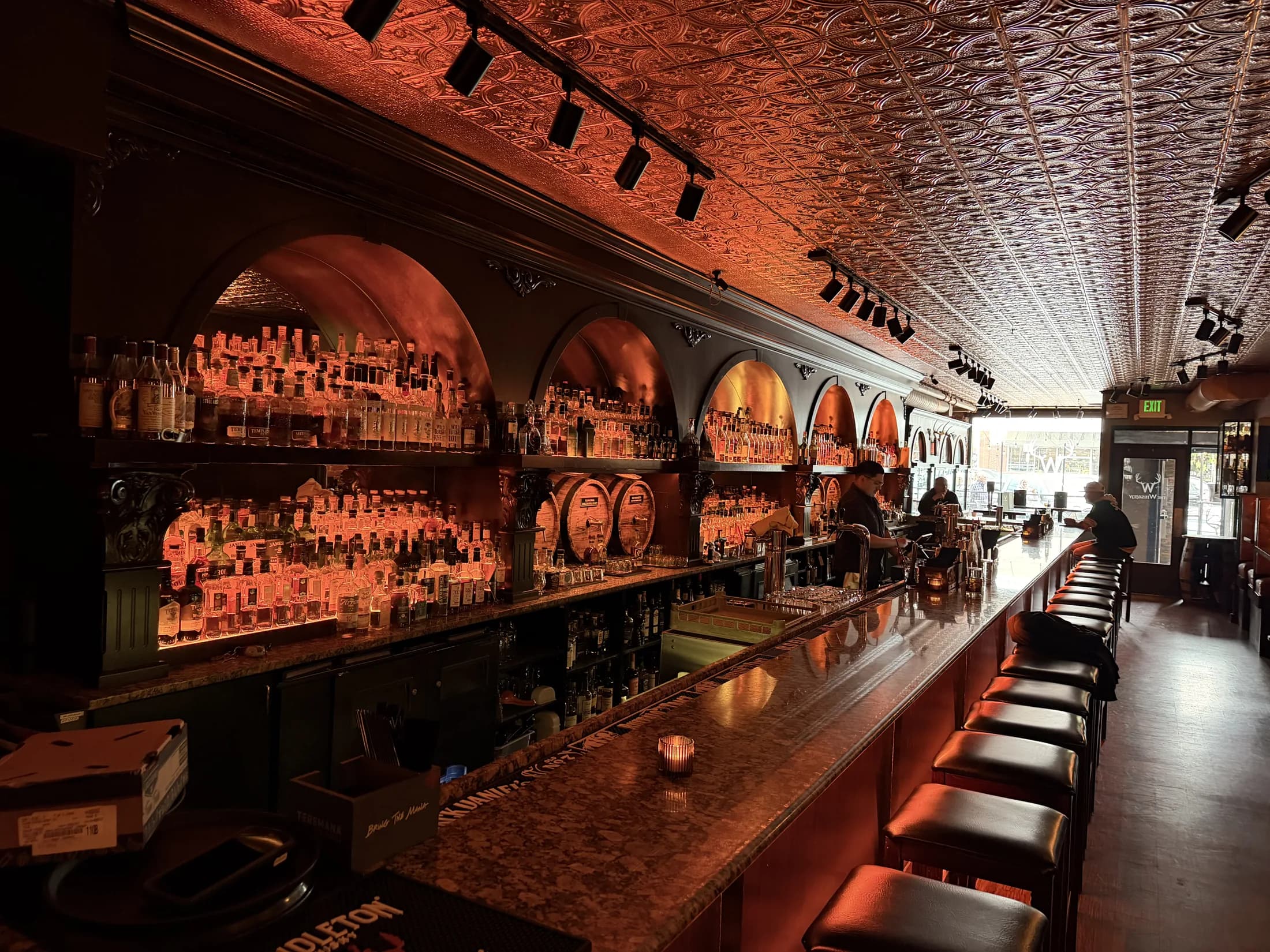 The Whisk(e)y's long bar under amber light, backbar arches full of bottles